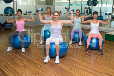 Fitness class holding dumbbells on exercise balls in studio