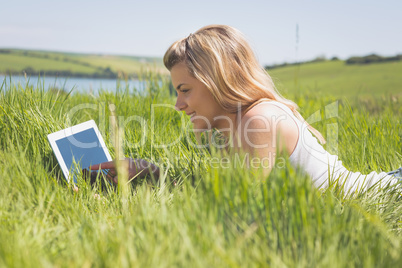 Pretty blonde lying on grass using her tablet