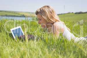 Pretty blonde lying on grass using her tablet