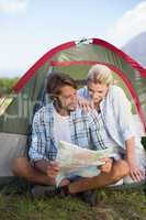 Attractive happy couple sitting by their tent reading map