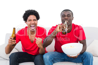 Football fans in red cheering on the sofa with beers and popcorn