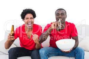 Football fans in red cheering on the sofa with beers and popcorn
