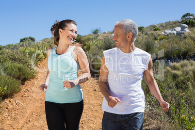 Fit smiling couple jogging down mountain trail