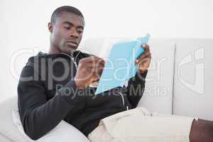 Casual man sitting on his sofa reading a book