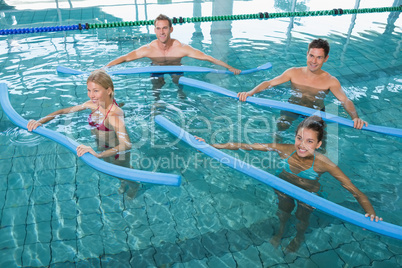 Happy fitness class doing aqua aerobics with foam rollers