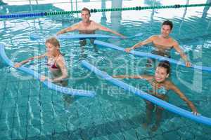 Happy fitness class doing aqua aerobics with foam rollers