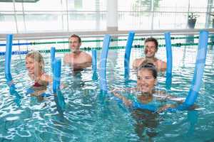 Happy fitness class doing aqua aerobics with foam rollers