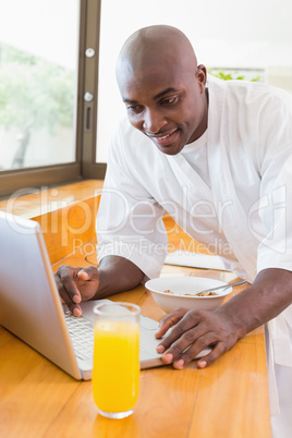 Happy man in bathrobe using laptop at table