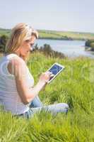 Pretty blonde sitting on grass using her tablet