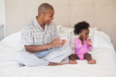 Father and baby girl sitting on bed together