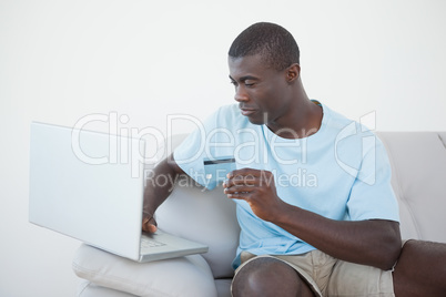 Casual man sitting on sofa using laptop to shop online