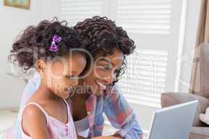 Cute daughter using laptop at desk with mother