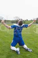 Disappointed football player in blue sitting on pitch after losi