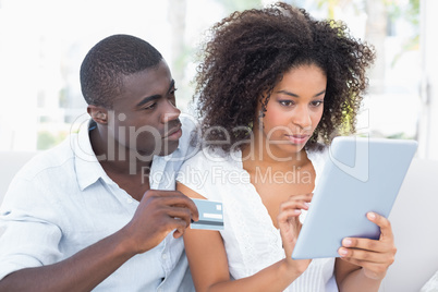Attractive couple using tablet together on sofa to shop online