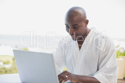 Handsome man in bathrobe using laptop at breakfast outside