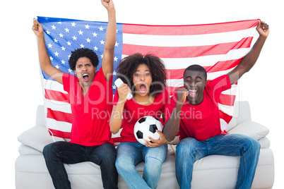 Cheering football fans in red sitting on couch with usa flag