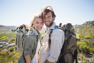 Hiking couple standing on mountain terrain smiling at camera