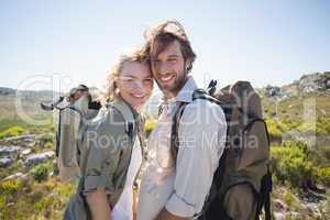 Hiking couple standing on mountain terrain smiling at camera