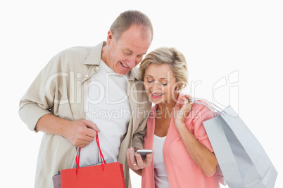 Smiling older couple holding shopping bags looking at smartphone