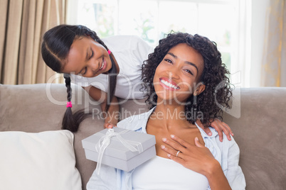 Pretty mother sitting on couch with daughter offering a gift