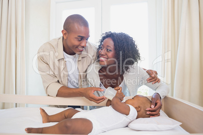 Happy parents feeding their baby boy in his crib