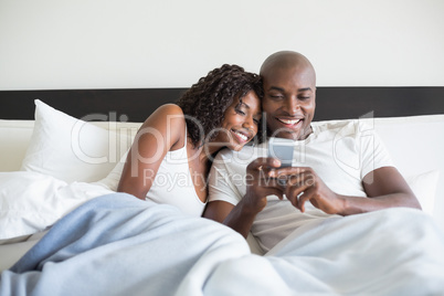 Happy couple cuddling in bed with smartphone