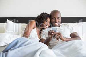 Happy couple cuddling in bed with smartphone