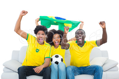 Excited football fans in yellow sitting on couch with brazil fla