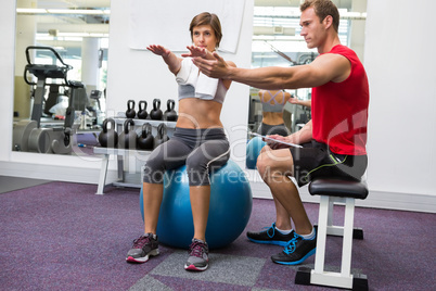Personal trainer with client sitting straight on exercise ball