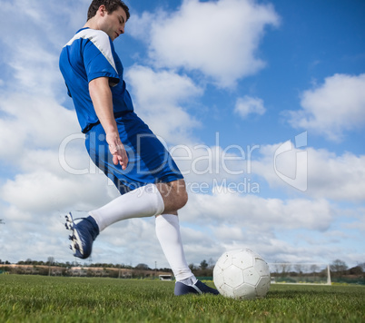 Football player in blue kicking the ball on pitch