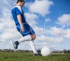 Football player in blue kicking the ball on pitch