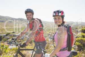Fit cyclist couple smiling at camera on mountain trail