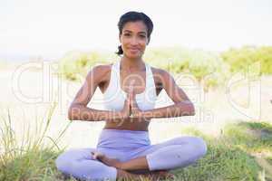 Fit woman sitting on grass in lotus pose smiling at camera