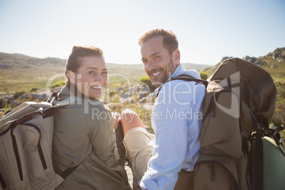 Hiking couple sitting on mountain terrain smiling at camera