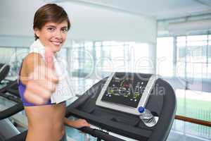 Fit brunette smiling at camera on the treadmill showing thumbs u