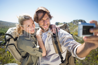 Hiking couple standing on mountain terrain taking a selfie