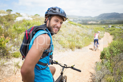 Fit couple cycling on mountain trail man smiling at camera