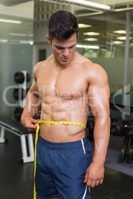 Muscular man measuring waist in gym