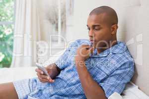 Thinking man sitting on bed and texting on phone