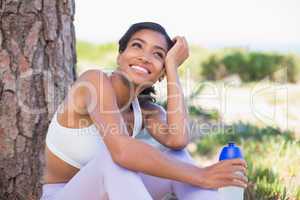 Fit woman sitting against tree holding water bottle