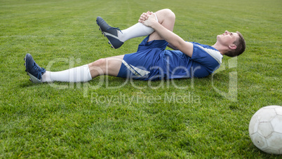 Football player in blue lying injured on the pitch