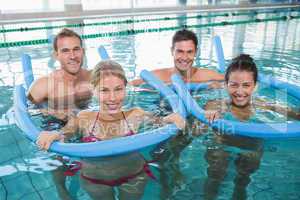 Happy fitness class doing aqua aerobics with foam rollers