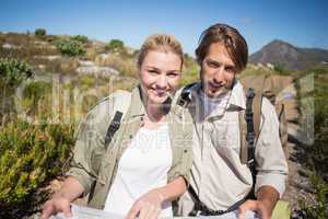 Hiking couple walking on mountain terrain holding map smiling at