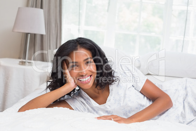 Pretty woman smiling at camera lying on bed