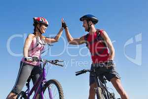 Fit cyclist couple standing at the summit high fiving