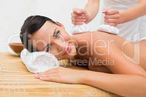 Beautiful brunette enjoying a herbal compress massage smiling at