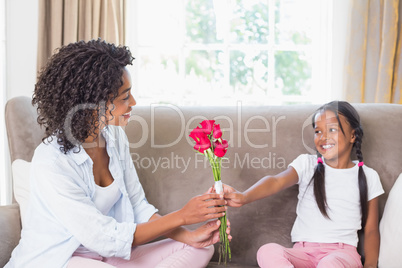 Pretty mother sitting on the couch with her daughter offering ro