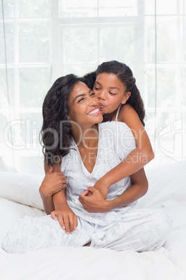 Smiling mother and daughter posing together on bed