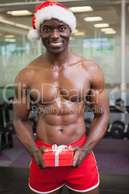 Shirtless macho man in santa hat holding gift