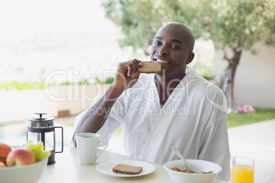 Handsome man in bathrobe having breakfast outside